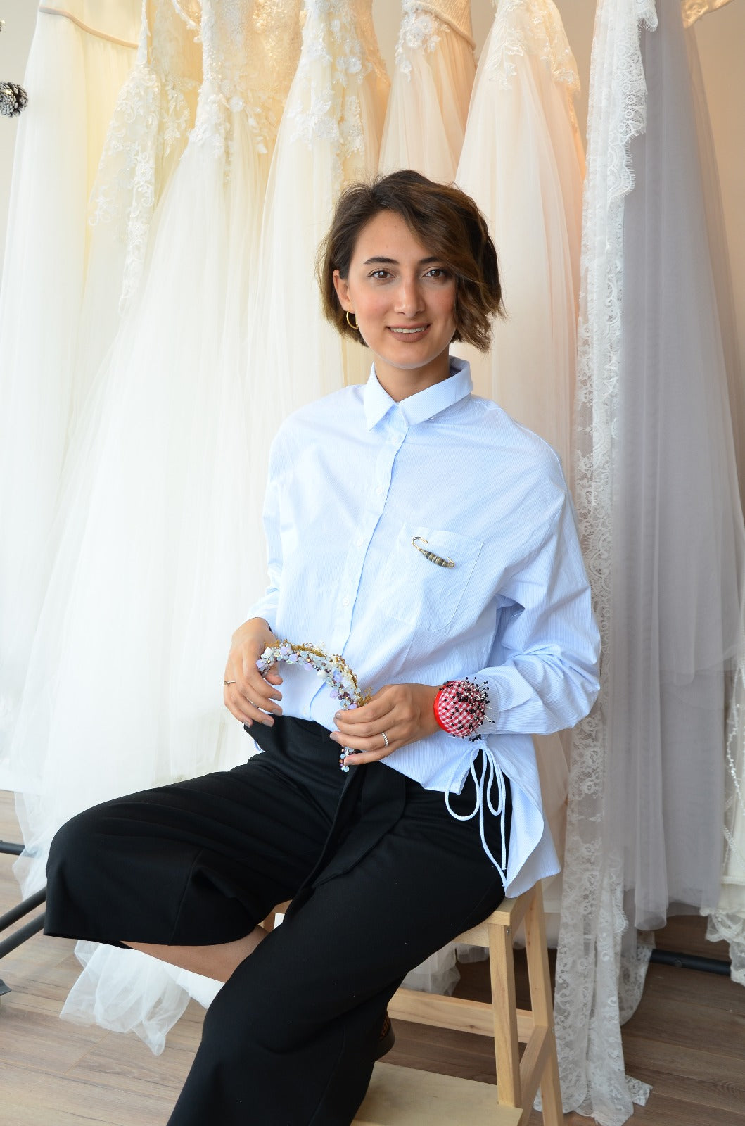 Gamze, founder and designer of Vowen, holding a beaded bridal hair vine in her studio beside hanging wedding gowns